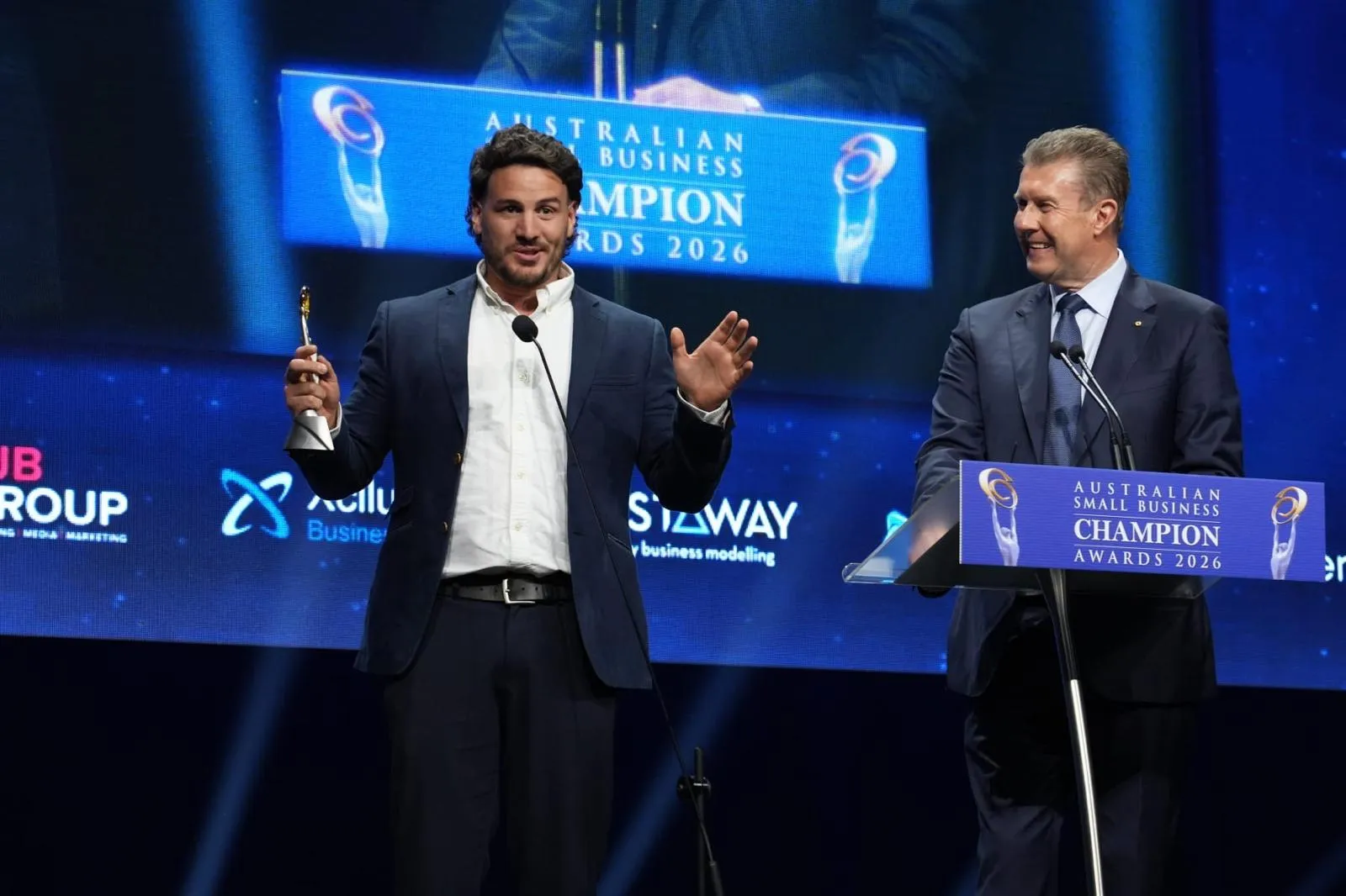 Manolo accepting the Removalist award on stage, trophy in hand, beside the presenter