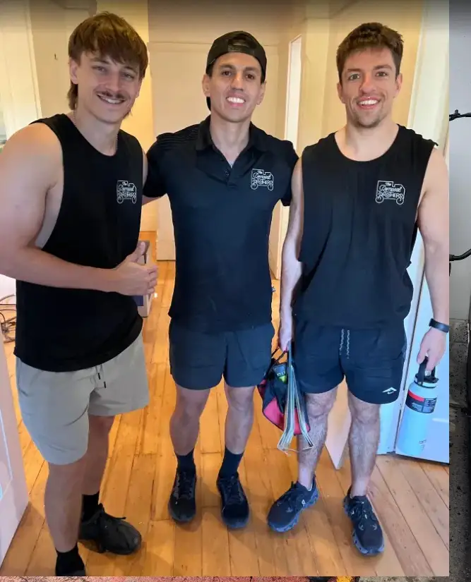 Three Removal Brothers crew in branded black uniforms standing in a hallway with timber floors at the end of a job