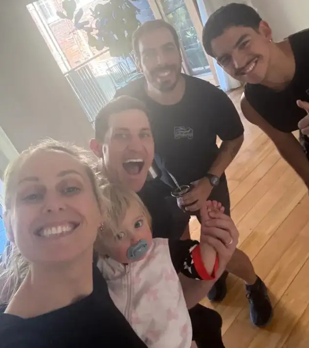 A customer holding a small child, photographed with three Removal Brothers crew in a bright room with timber floors