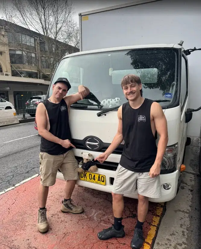 Two Removal Brothers crew standing at the front of a branded truck parked on a Sydney street